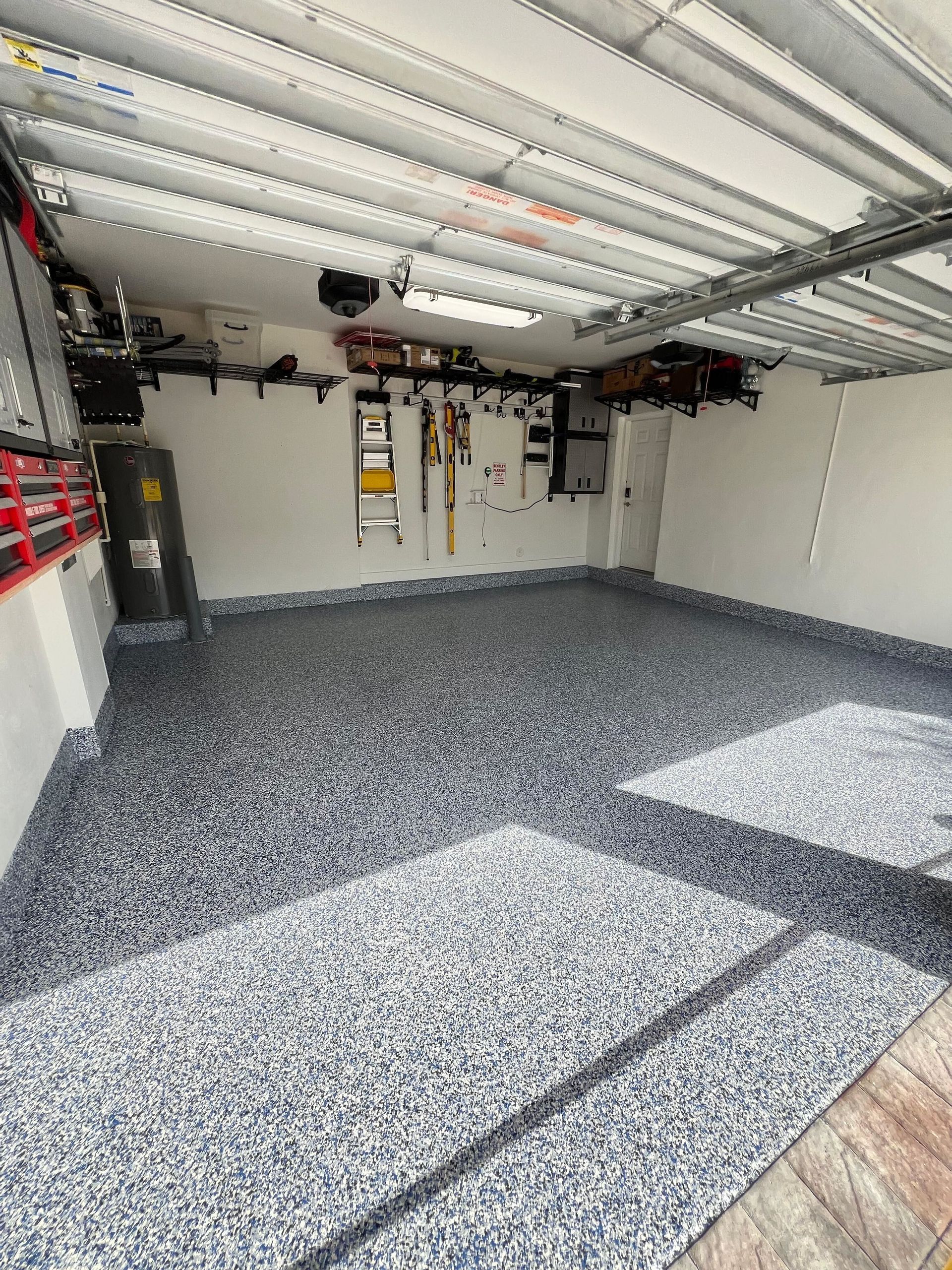 Empty garage with speckled epoxy floor, open door, and wall-mounted tools and storage.