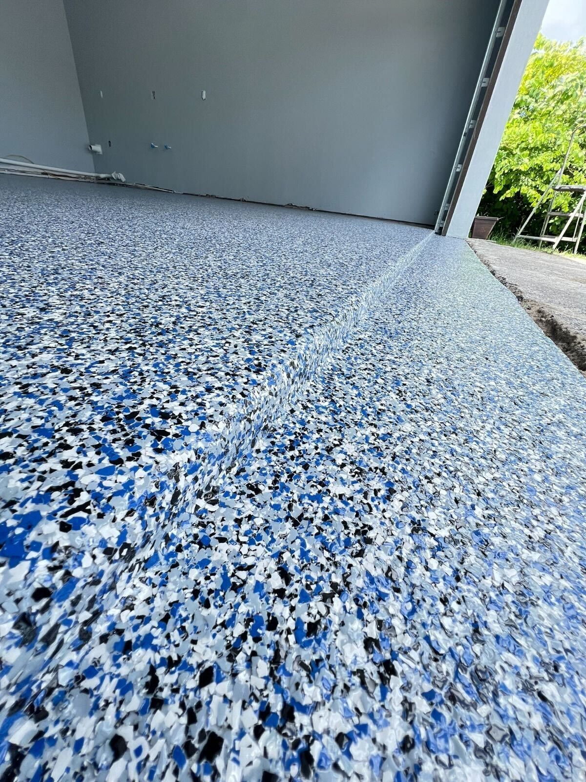 Blue-and-white speckled epoxy floor beside a gray wall and doorway, viewed from ground level