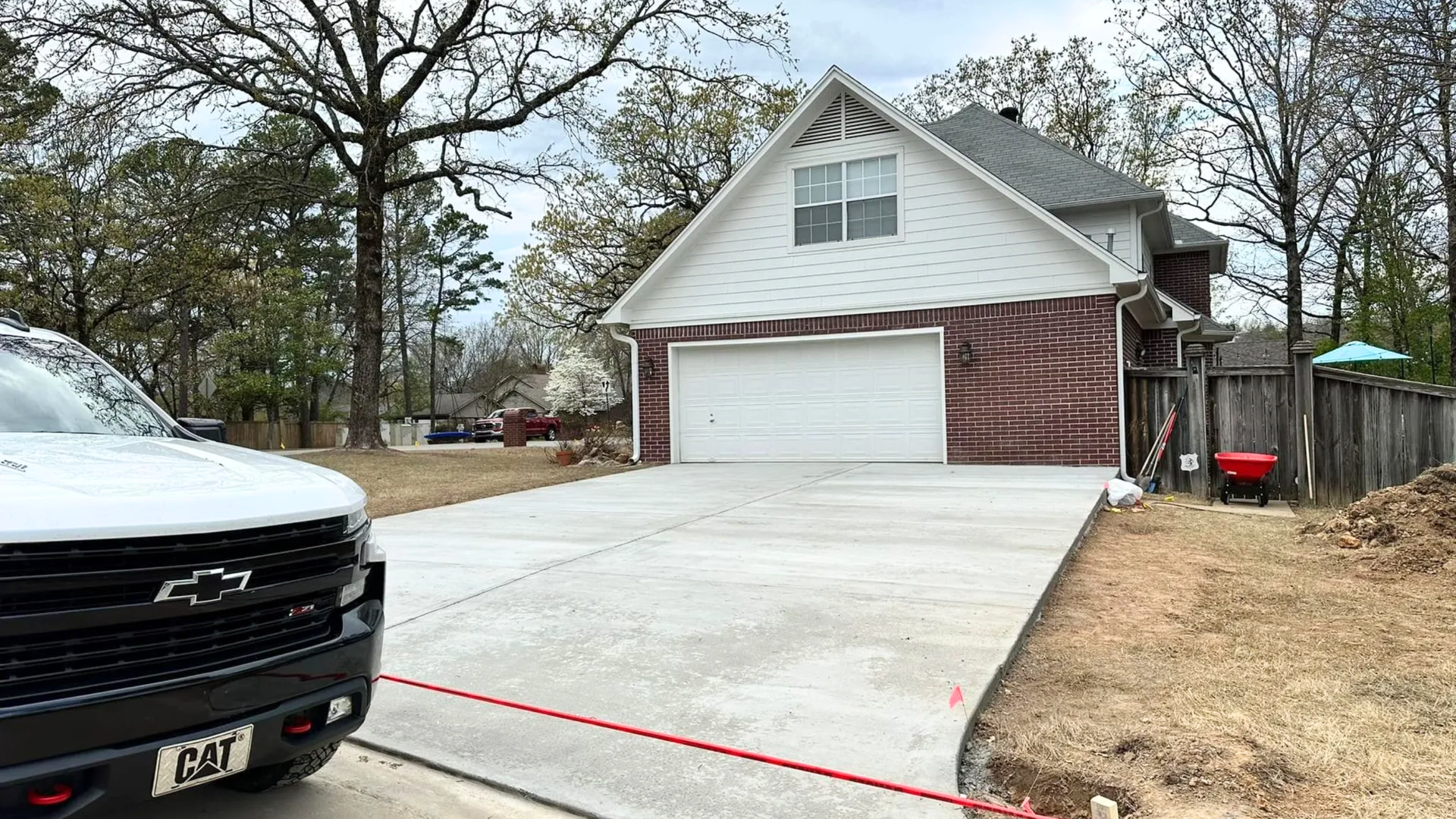 Driveway leading to a white-and-brick house with a two-car garage and a black truck in the foreground.