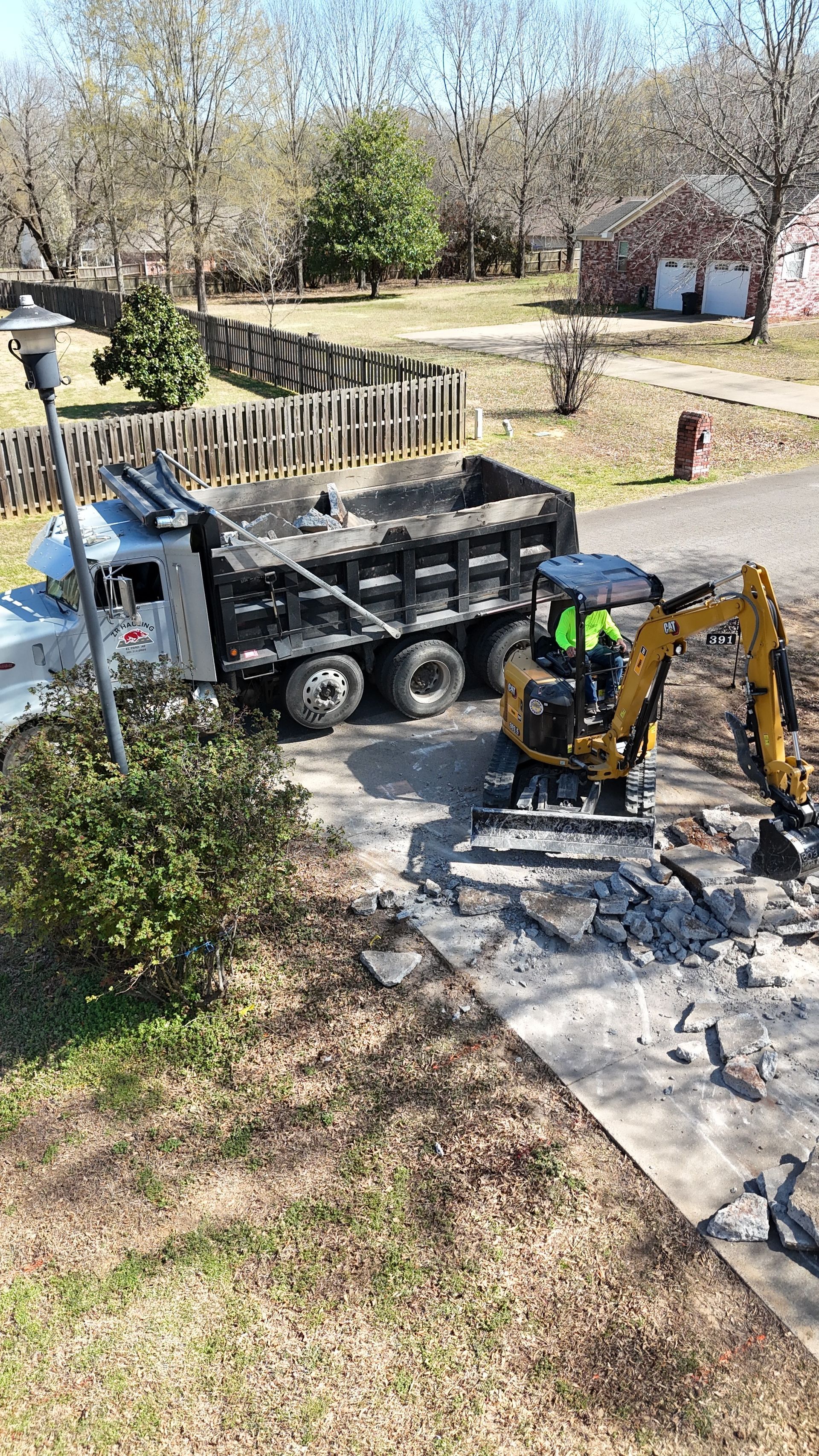 Backhoe and dump truck working on a gravel driveway in a suburban yard