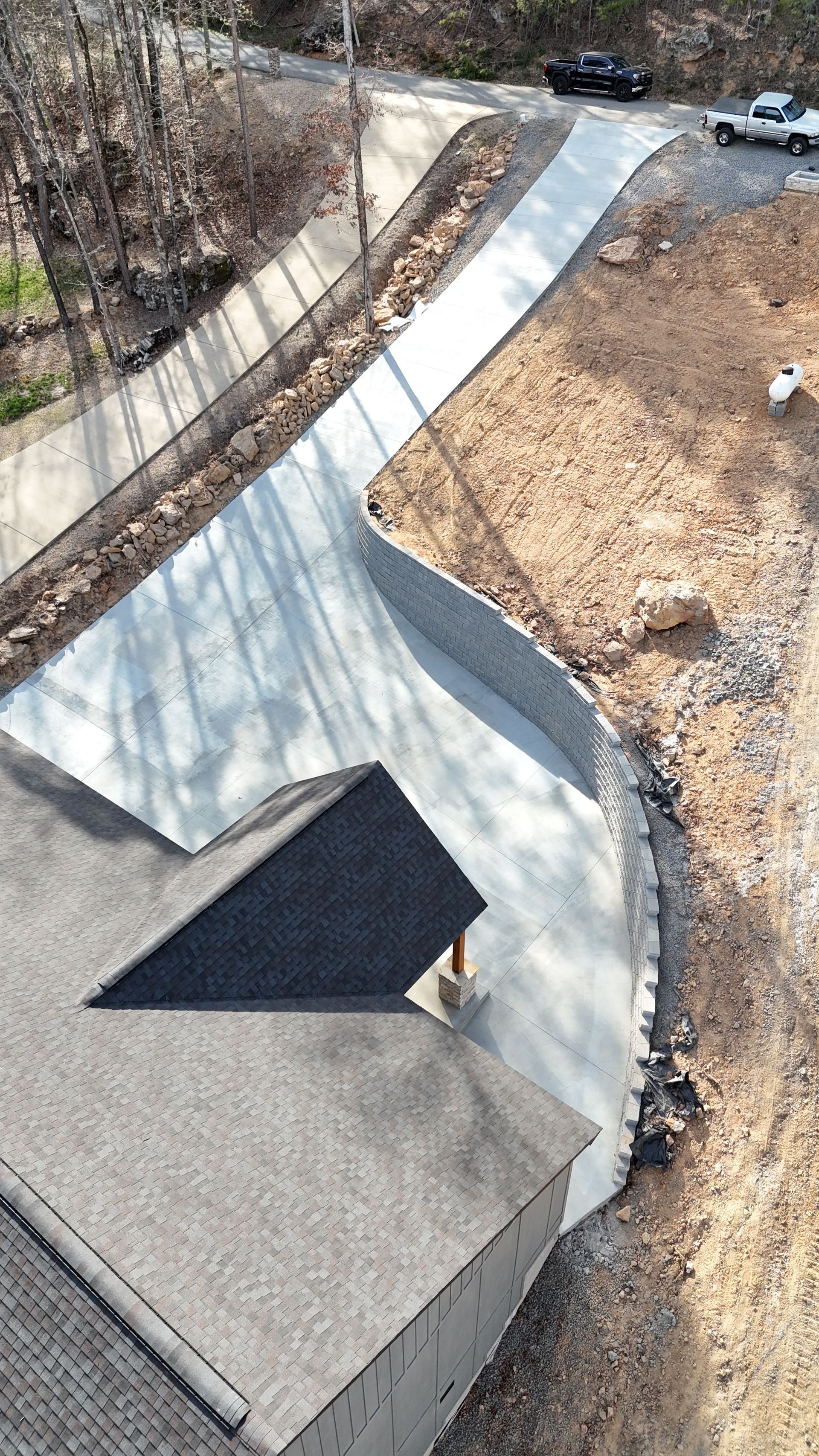 Concrete driveway and walkway curving uphill beside a house, with dry grass and trees nearby