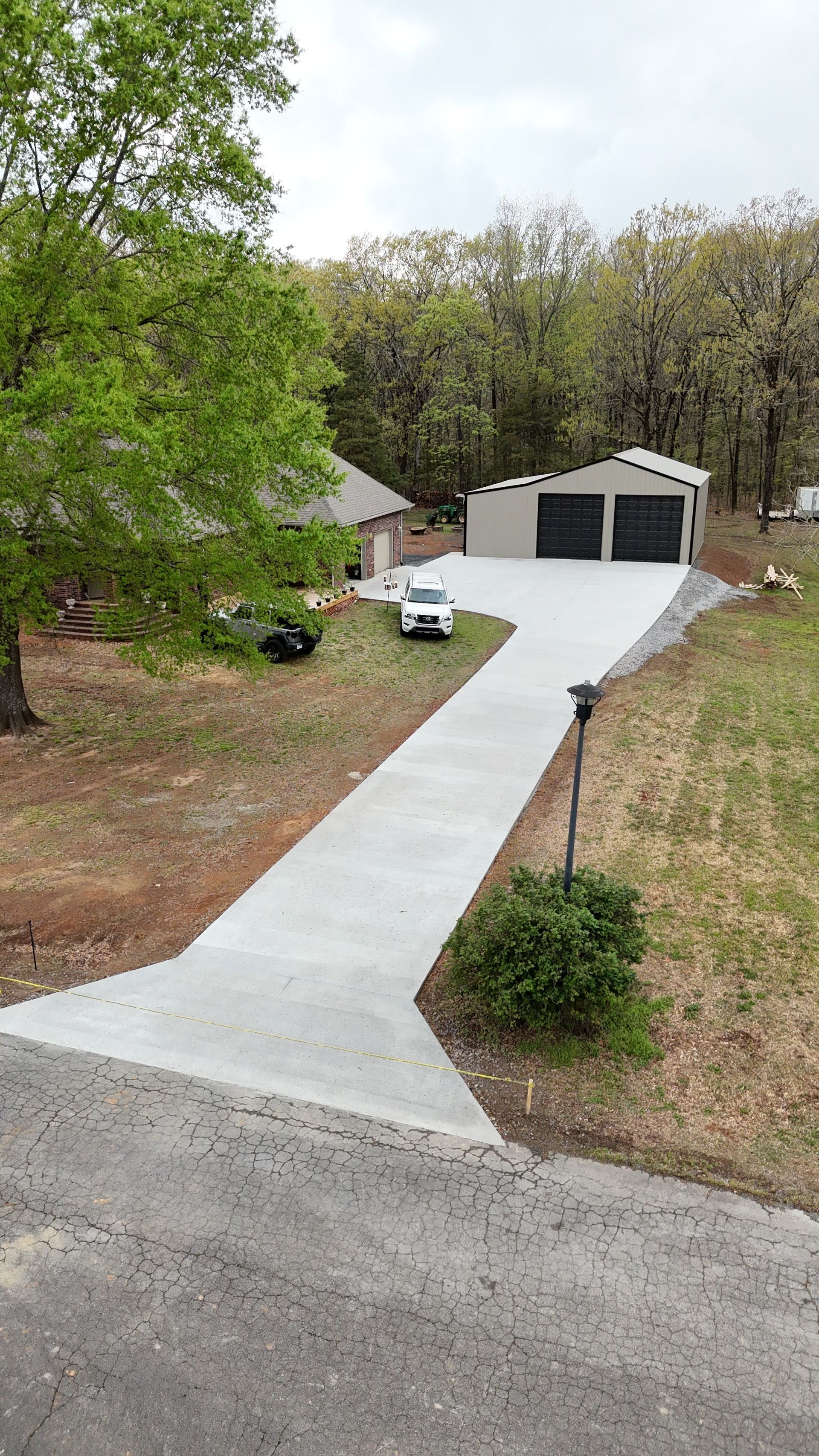 Concrete driveway leading to a two-car garage with trees and a landscaped yard on both sides