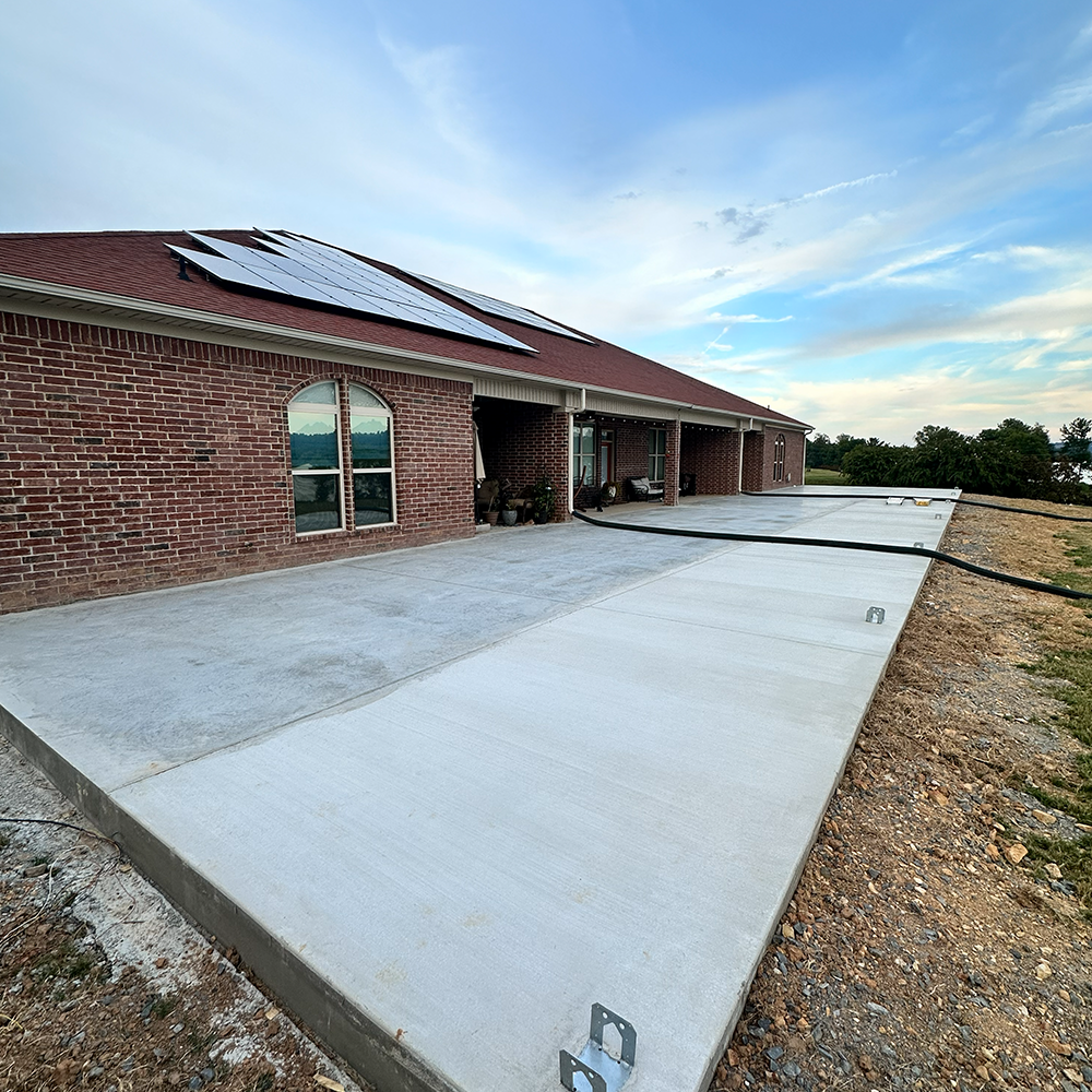 Brick house with solar panels and a wide concrete driveway under a blue sky