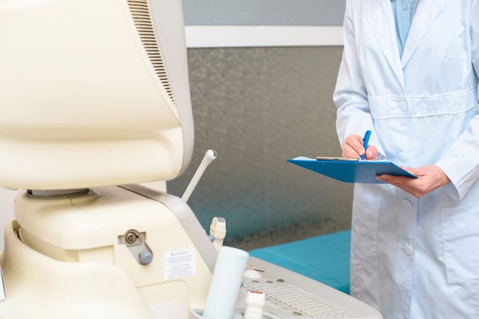 Un operatore sanitario tiene in mano una cartella clinica blu accanto a una sedia da visita in una stanza clinica.
