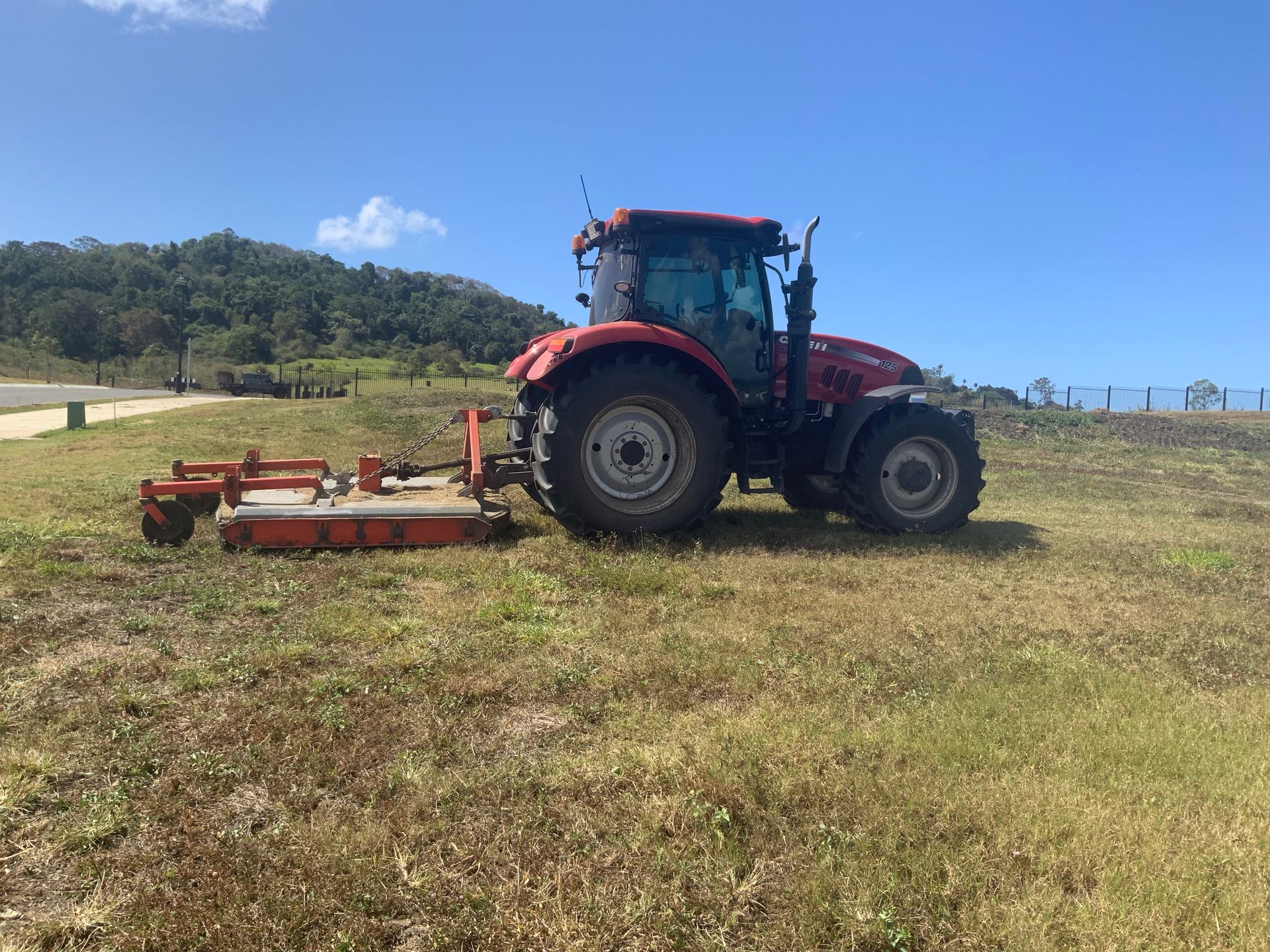 Red Tractor Mowing Grass in a Sunny Field With Hills — Cane Country Slashing & Mowing In Marian, QLD