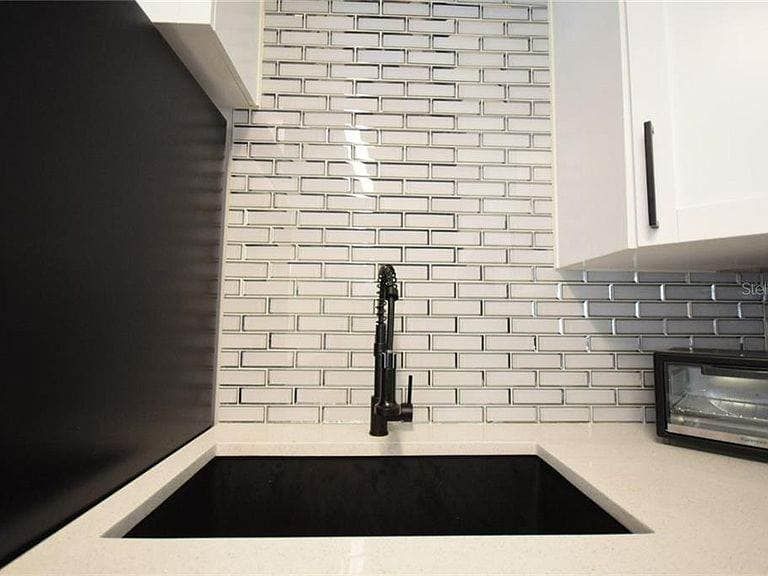 A kitchen sink with a black faucet and a brick wall behind it.
