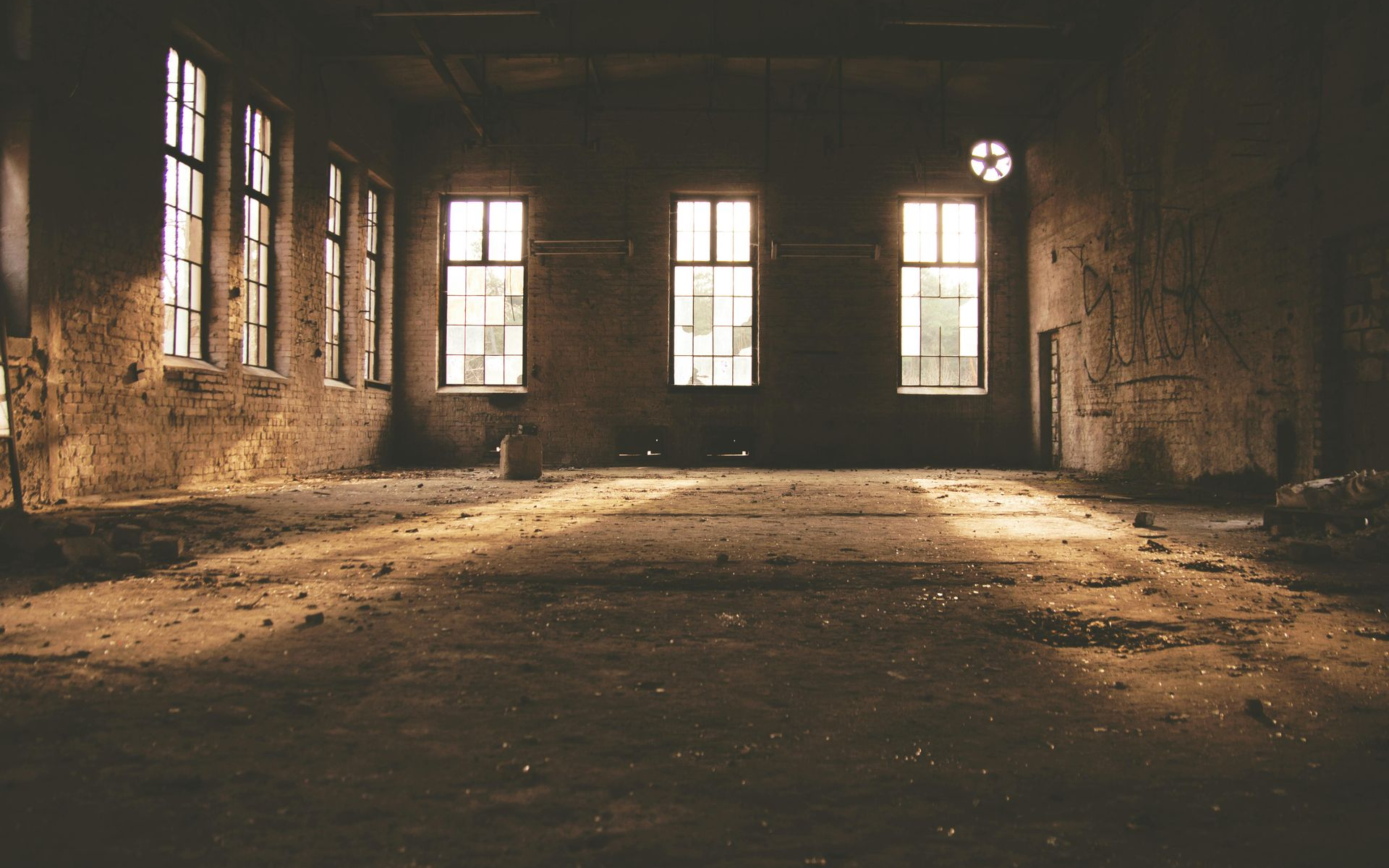 Sunlight streams into a dark, empty, industrial room with windows and weathered walls.