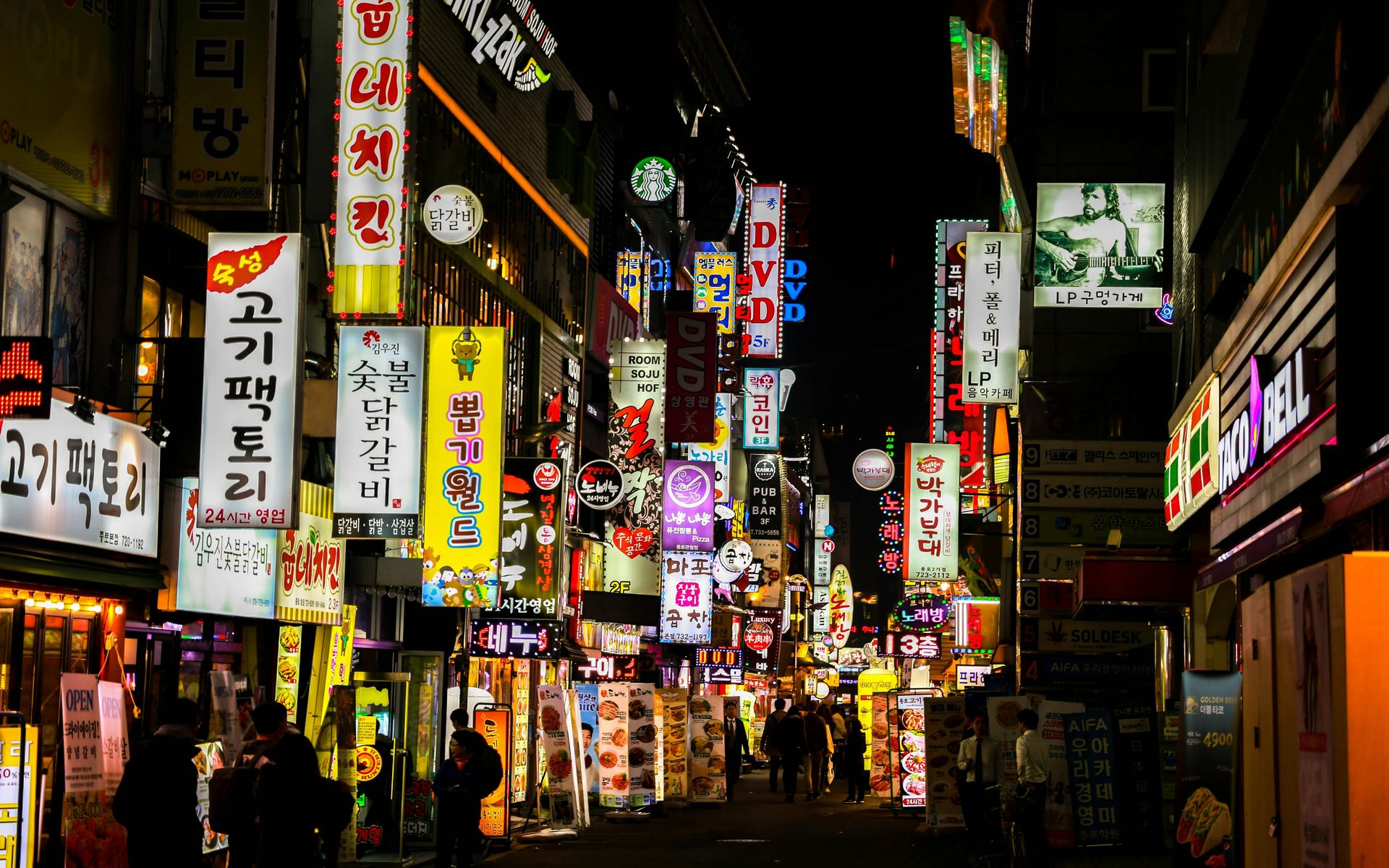 Night scene in Seoul, South Korea; neon signs illuminate a street filled with shops and pedestrians.