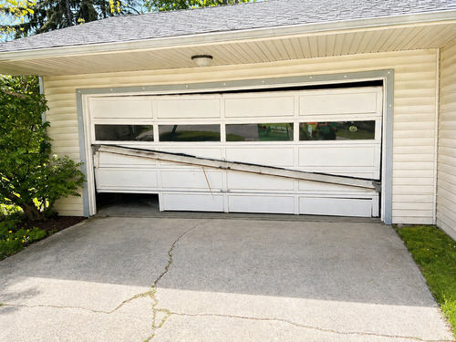 A hand holds a remote control, operating a white paneled garage door as it rises in front of a stone-faced building.