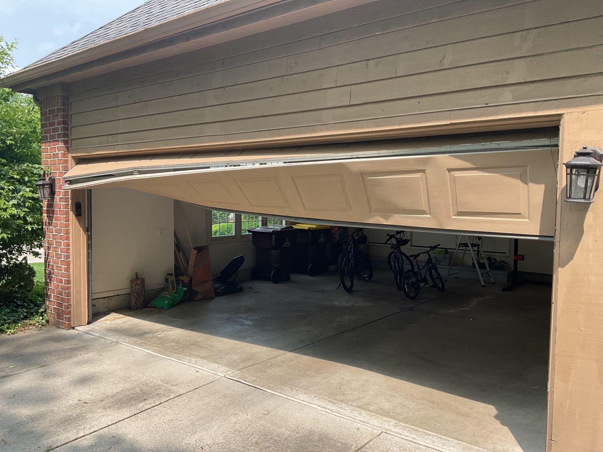 Partially open garage with a white door, bicycles inside, and a concrete driveway in front. Partially open garage with a white door, bicycles inside, and a concrete driveway in front.