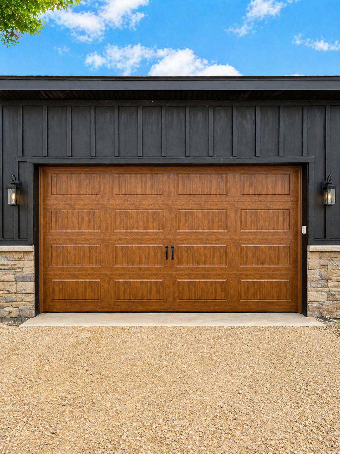 Two gray multi-panel garage doors set in a cream-colored stone house exterior on a sunny day.