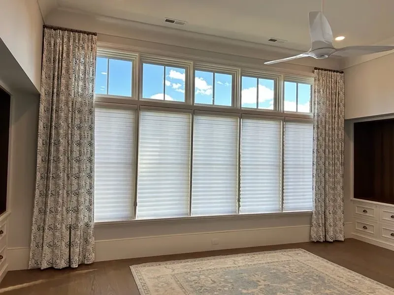 Large, multi-paned window wall with white pleated shades and patterned curtains in a bright, modern room.