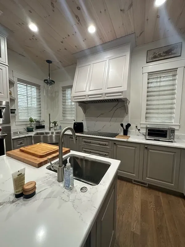 A bright kitchen with white cabinets, a large farmhouse sink, marble-style countertops, and light-toned wood ceiling.