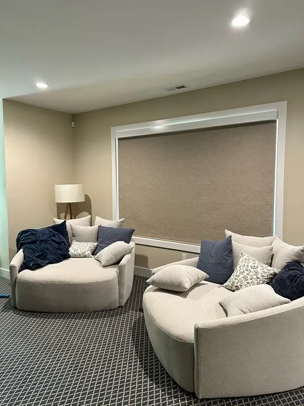 Two large, round, cream-colored armchairs with navy and patterned throw pillows sit on a patterned carpet in a room.