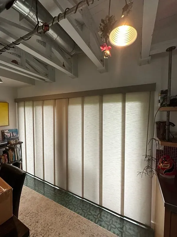A large sliding panel shade covering a wall-to-wall glass door in a brightly lit room with a patterned floor.