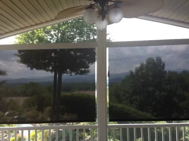 A covered porch overlooking a scenic landscape of trees and hills, partially obscured by two dark mesh privacy screens.