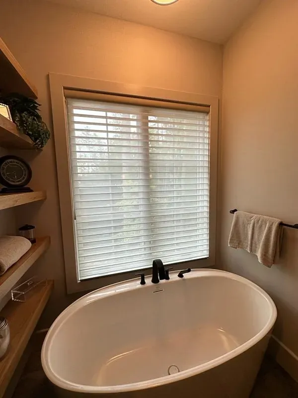 Small bathroom with a freestanding tub, window blinds, shelves, and a towel rack.