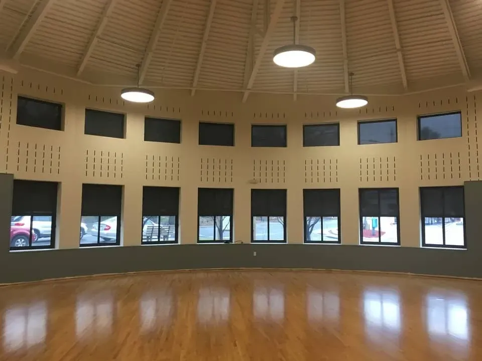 A spacious, circular room with wooden floors, neutral walls, and a row of windows topped by rows of small decorative vents.