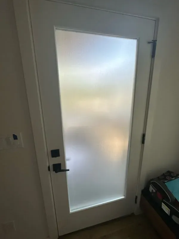 A white door with a large, rectangular frosted glass window and a black handle and deadbolt.