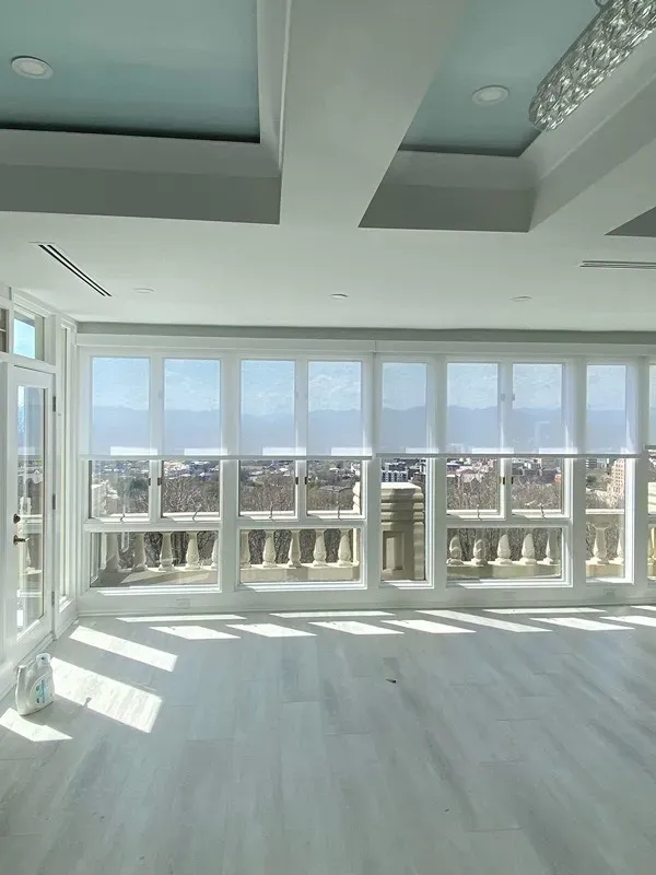 A sunlit, minimalist room with light wood floors and a large wall of windows overlooking a distant mountain view.