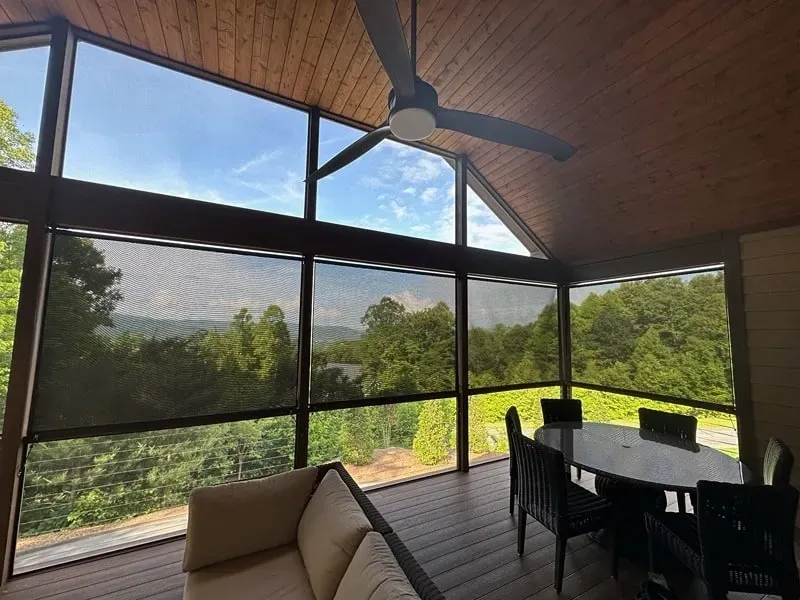 Screened porch with sofa and dining table, wood ceiling, large windows, and mountain view.