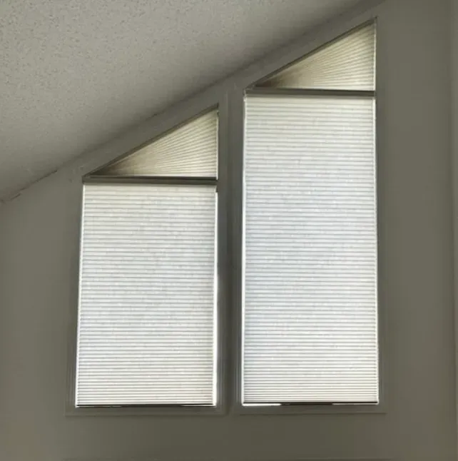 Two white blinds in a slanted ceiling window, one shorter and one taller, letting in diffused light