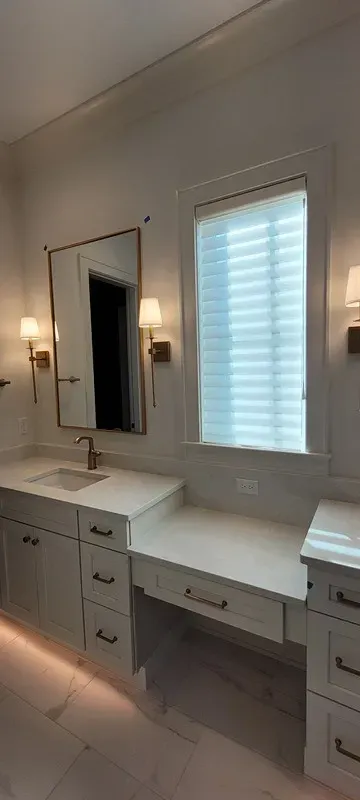 A bathroom vanity with a white countertop, gold hardware, wall-mounted sconces, and a rectangular mirror.