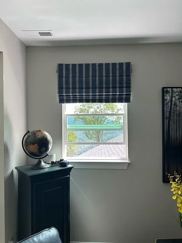Small room with a window, blue plaid valance, black cabinet, globe, and a wall mirror.