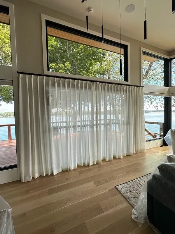 Floor-to-ceiling white sheer curtains hang in front of large windows overlooking a lake and wooden deck.
