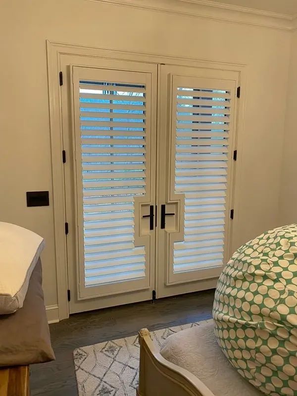 White double doors with horizontal window shutters, black hardware, and geometric frame detail in a neutral-toned room.