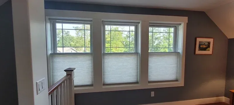 Three white-trim windows with blinds in a gray room, viewed from an upstairs landing