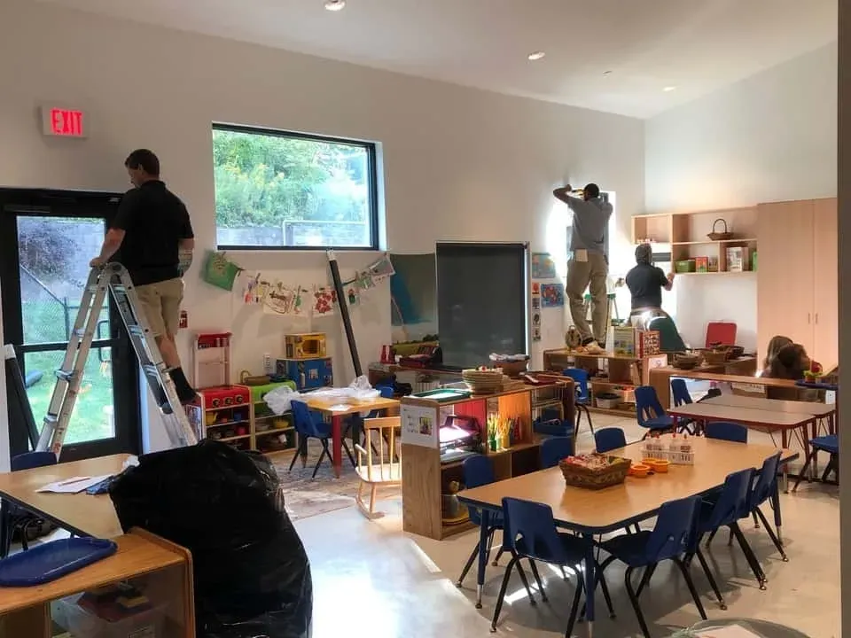 People painting a classroom with tables, chairs, and children’s art supplies