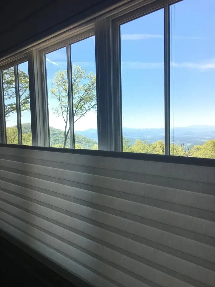 A scenic mountain view framed by windows, partially obscured by horizontal pleated shades.