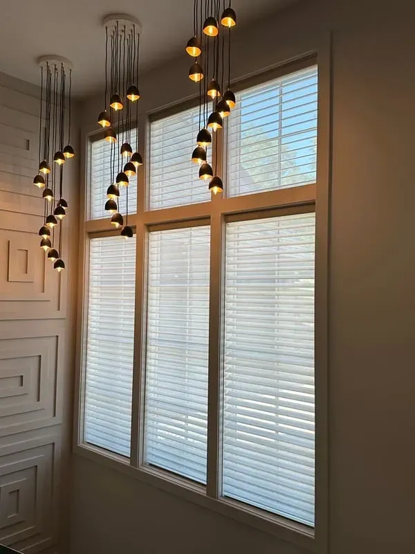Three clusters of hanging pendant lights illuminate a large, multi-paned window with horizontal white blinds.