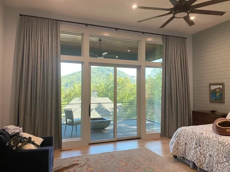 A bedroom features floor-to-ceiling gray curtains framing a sliding glass door with a scenic mountain view.