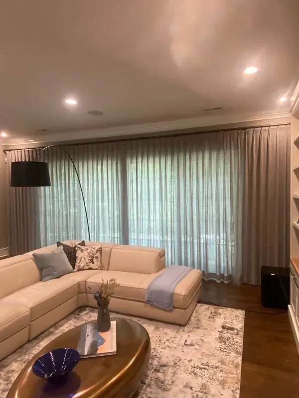 A cozy living room with a beige sectional sofa, a modern oval coffee table, and large curtains covering a wide window.