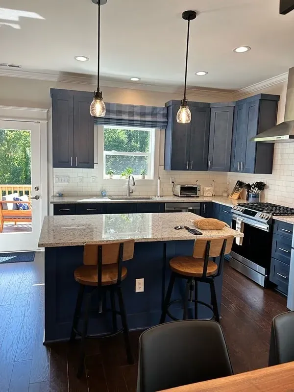 A kitchen featuring dark blue cabinets, a granite-topped island with two wooden stools, and modern hanging pendant lights.