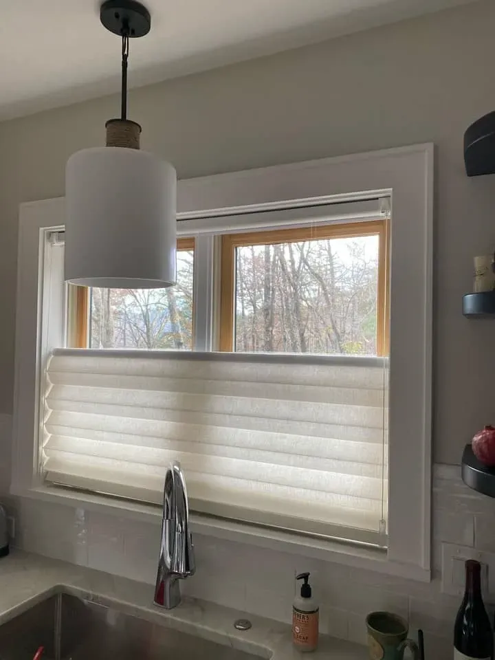 A kitchen sink area features a white pendant light hanging over a window covered by a pleated, top-down bottom-up shade.
