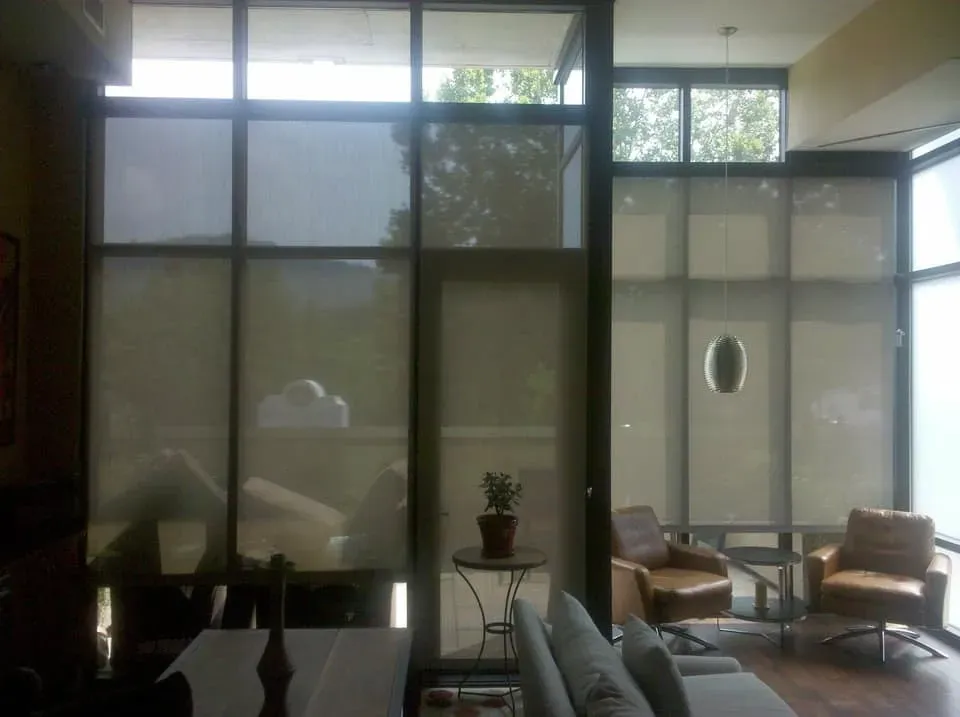 A living area with a large window wall, two leather armchairs, a side table with a plant, and a sofa in the foreground.