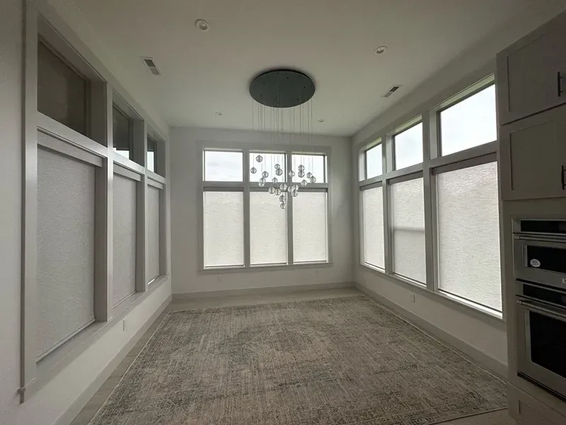 A dining room with large windows, light gray walls, a neutral rug, and a modern tiered glass chandelier.