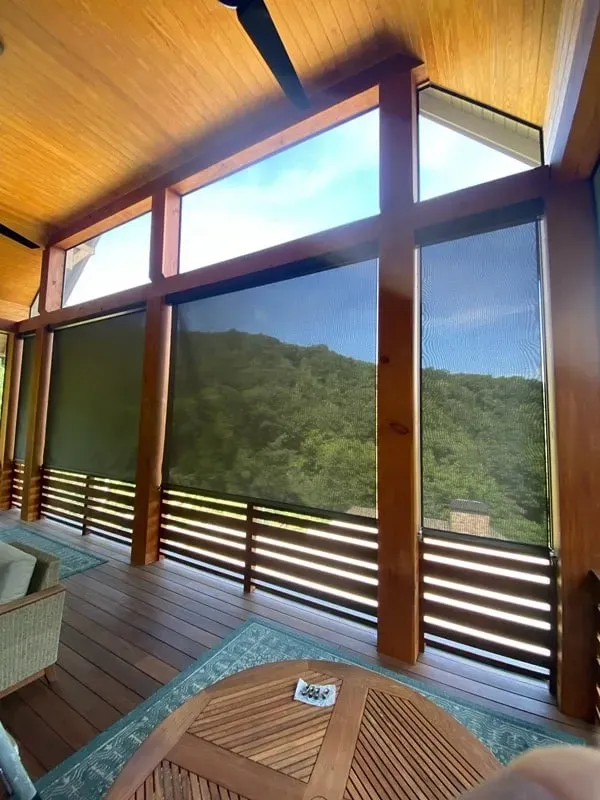 A wooden patio with roller shades looking out onto a forested mountain landscape.