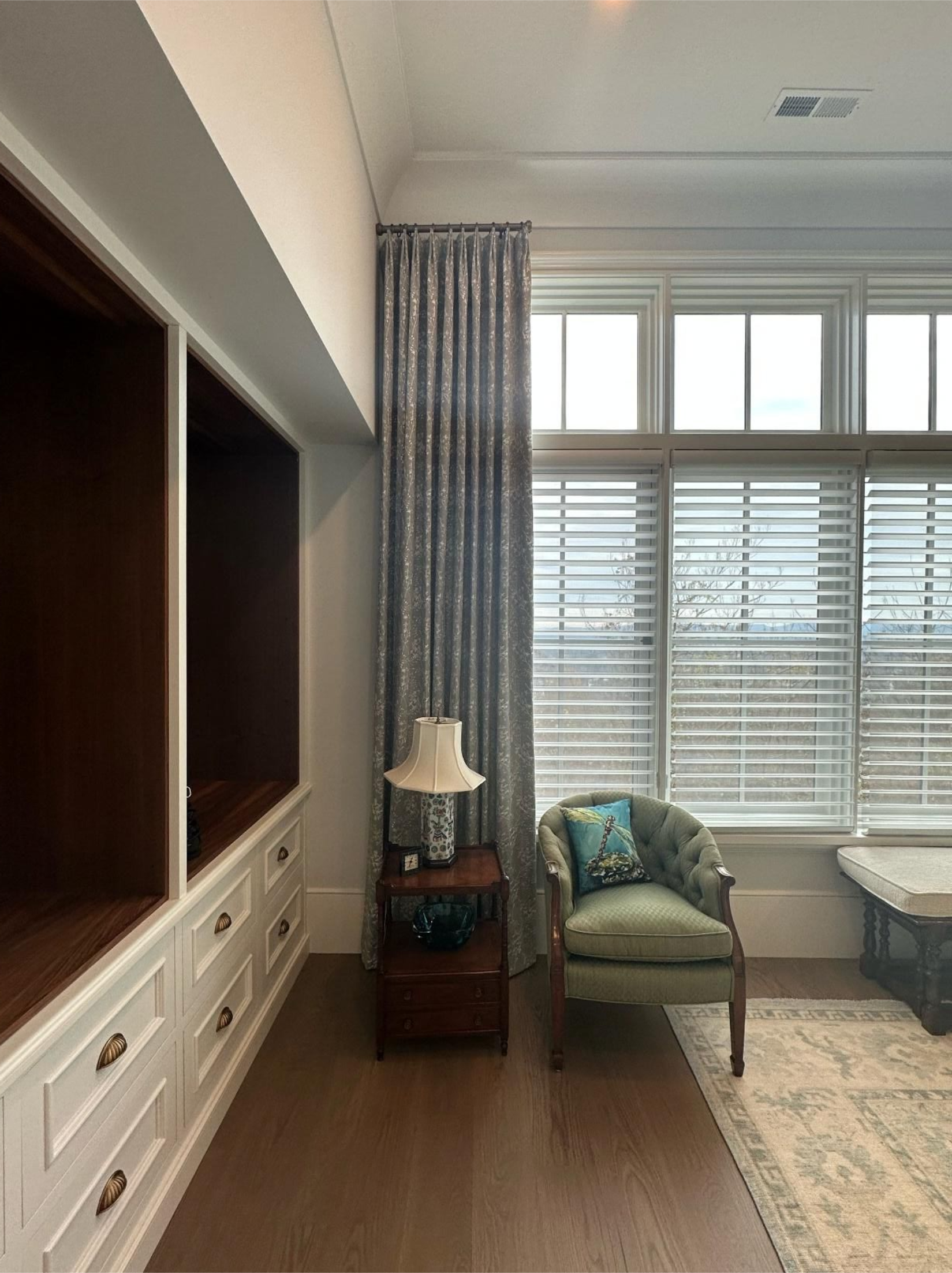 Bright bedroom with white dresser, green chair, lamp, bay window, and patterned rug.