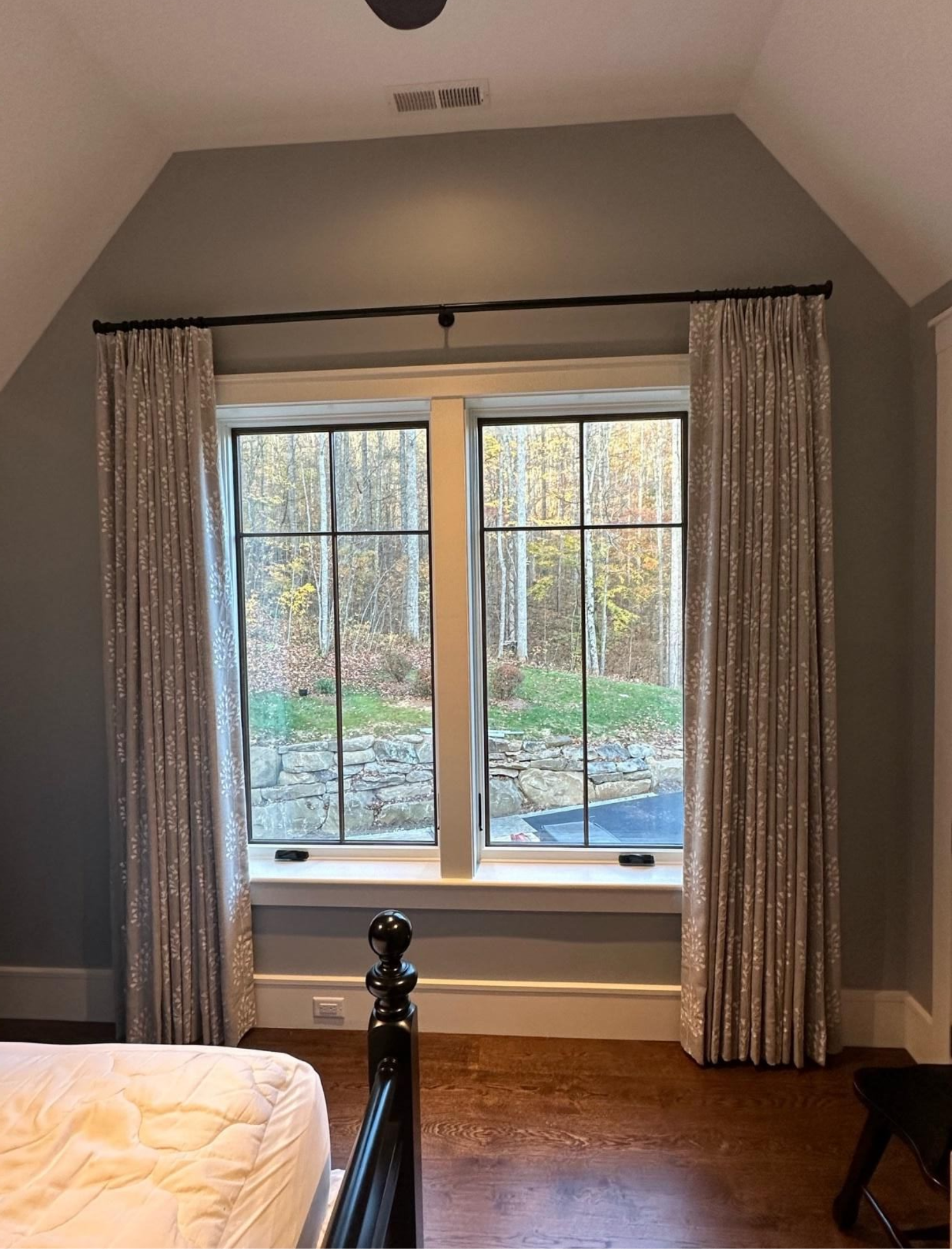 Bedroom with a large window, gray walls, curtains, and a view of trees outside.