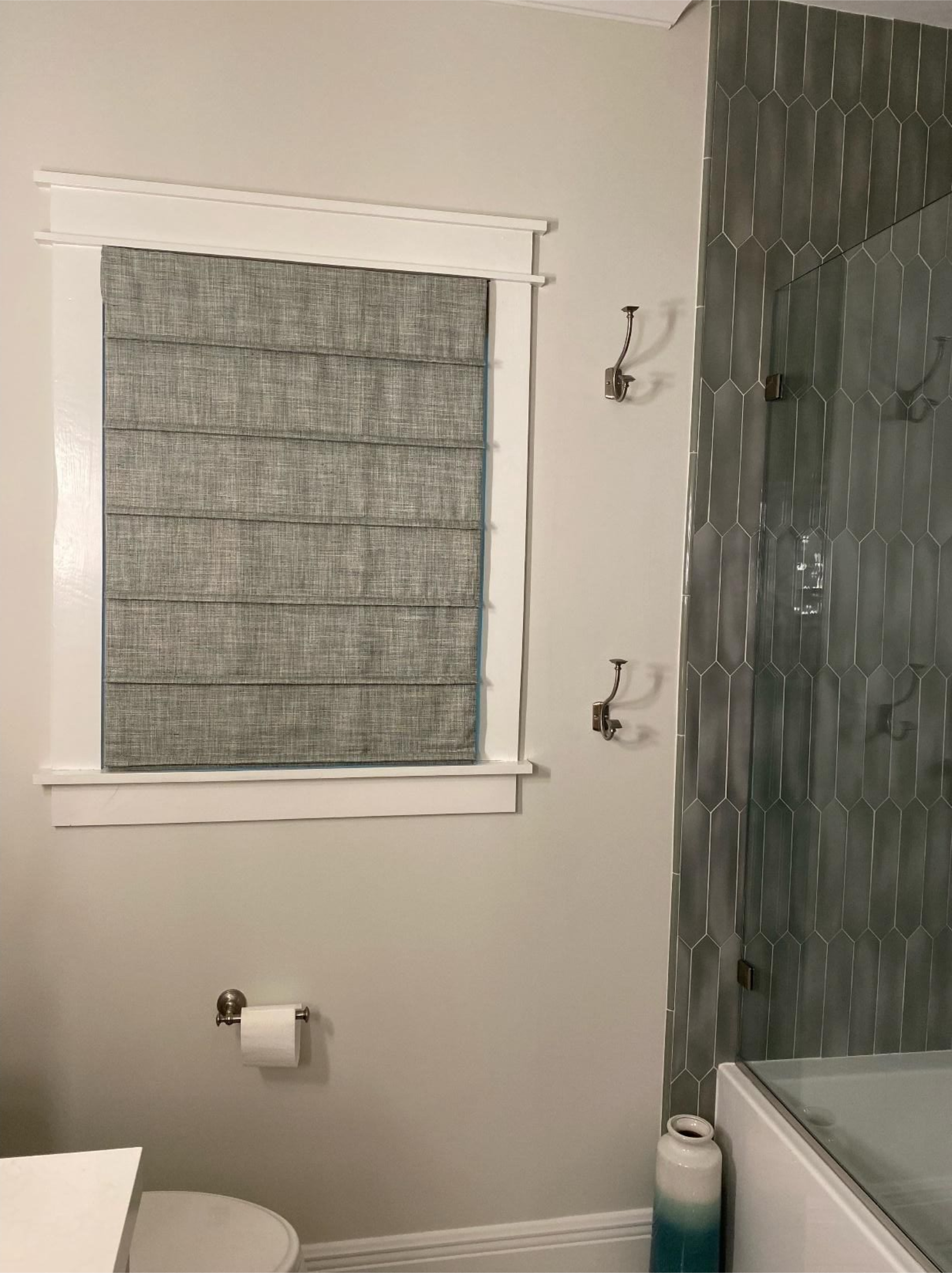 Small bathroom with frosted window, toilet paper holder, shower wall, and bathtub edge.