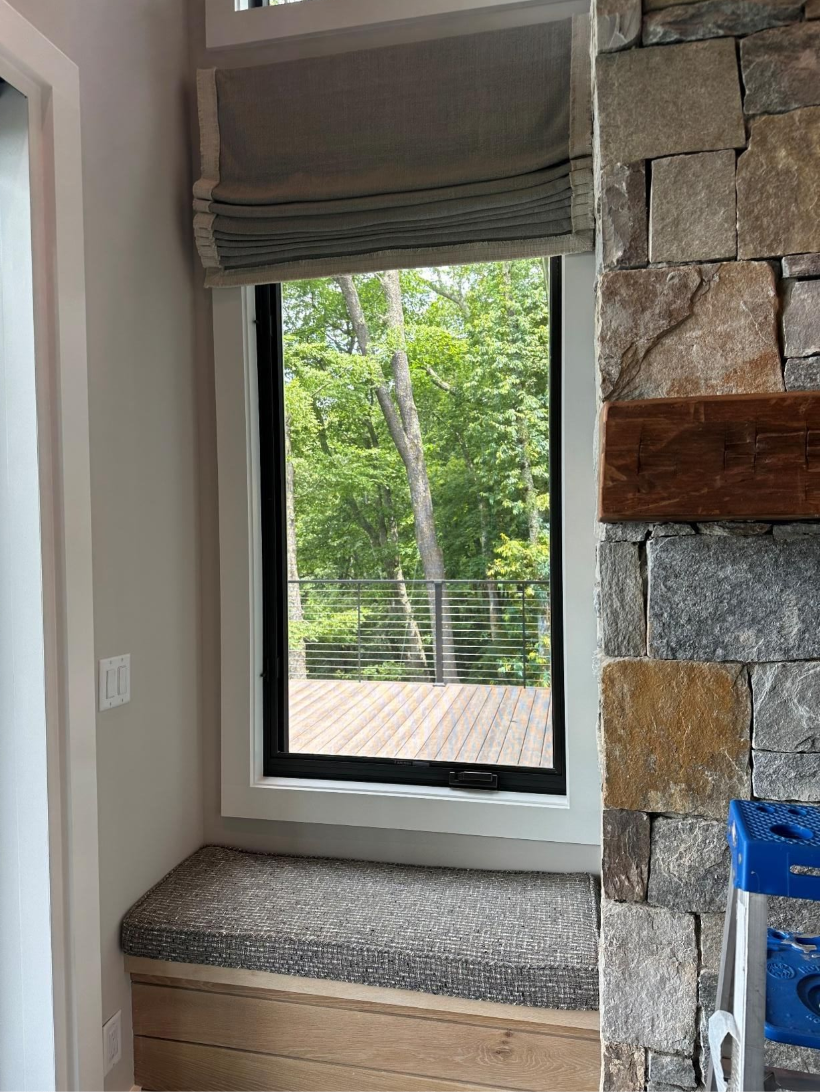 Window seat with patterned cushion beside a stone accent wall, overlooking greenery outside