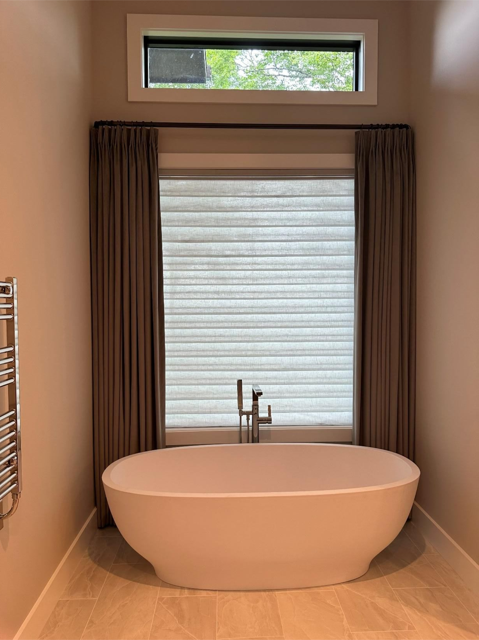 Modern bathroom with freestanding oval tub, window shades, and a small transom window