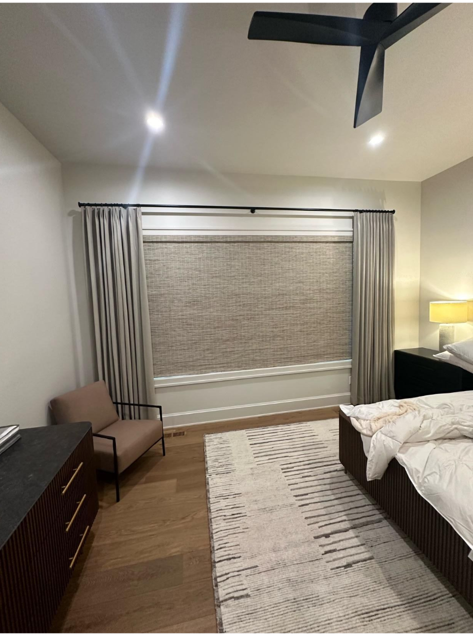 Bedroom with bed, chair, large window blinds, rug, and ceiling fan in warm lighting