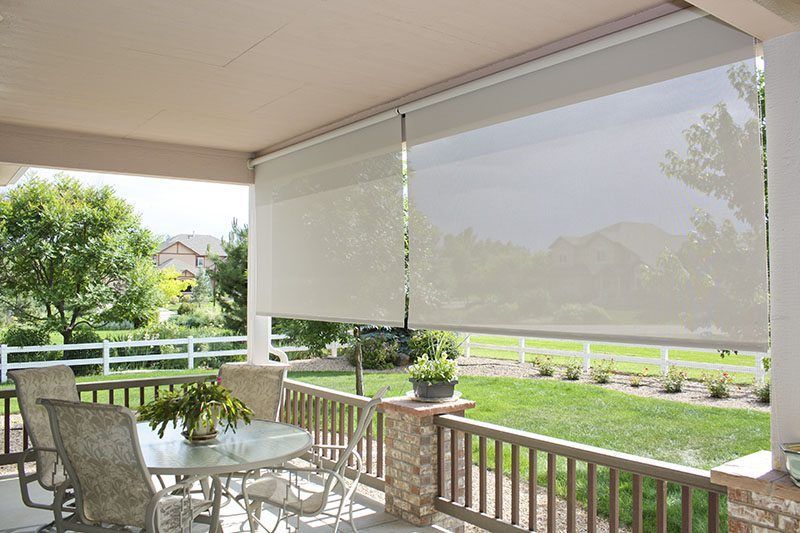 A modern white balcony features three windows with sun shades, wooden flooring, potted greenery, and orange flowers.