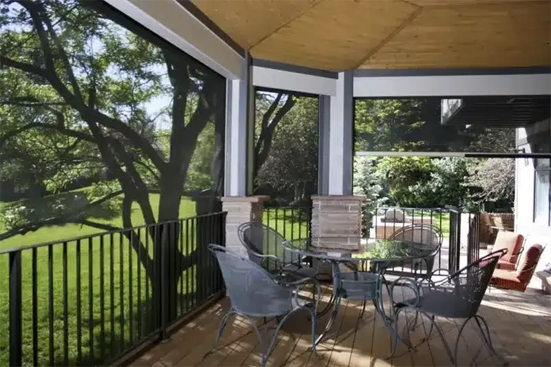 A covered outdoor deck featuring a glass dining table, chairs, and mesh screens overlooking a grassy yard with trees.