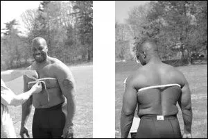 Man being measured, front and back views. Outdoors in green grass. He smiles in front view.